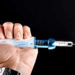 Hand holding a syringe with needle, promoting injection-free anesthesia for hair treatments.